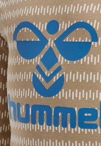 Bruine stof met witte verticale strepen en een groot blauw logo met een gestileerd bijenontwerp en de merknaam "hummel" in blauw.