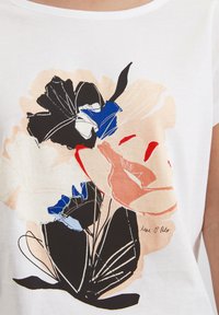 Witte t-shirt met een bloemmotief met zwarte, blauwe en rode accenten. Zachte stof met een ronde halslijn en korte mouwen.