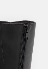 Black leather boot with a zipper on the side, featuring a smooth texture and closely stitched seams. The opening is wide and straight-edged.