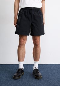 Black shorts made of lightweight fabric, featuring an elastic waistband, side pockets, and a discreet logo on the left leg.