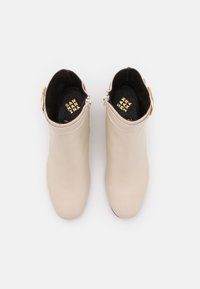 Beige kožené kotníkové boty s hladkým povrchem, bočním zipem a zlatým přezkovým detailem. Černá stélka s viditelným logem.