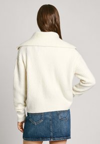 Crème geribbelde trui met een brede kraag, gecombineerd met een denim minirok. De trui heeft lange mouwen en een relaxte pasvorm.