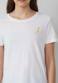 Witte katoen t-shirt met een kleine gele banaan borduring op de borst, ronde halslijn en korte mouwen. Zachte textuur, casual pasvorm.