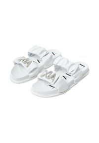 Sandali bianchi slip-on con cinturini in tessuto arricciato, dotati di un accento di logo metallico e un design a suola piatta. Texture liscia e stile minimalista.