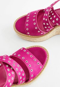 Espadrilky z fuchsiového semišu s prekrižovanými popruhmi, striebornými kovovými očkami a tkanou jutovou podrážkou. Ploché stielky s textúrovaným povrchom.