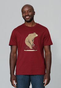 T-shirt à manches courtes maroon avec un graphisme d'un ours faisant du vélo rouge. Tissu doux avec un col rond et une coupe décontractée.