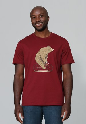 Bordeauxkleurig T-shirt met korte mouwen met een afbeelding van een beer die op een rode fiets rijdt. Zachte stof met een ronde hals en een ontspannen pasvorm.