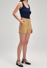 Marineblå, ribbet tanktop sat sammen med højtaljede beige shorts. Sorte, lakerede sko med blokhæle og guldfarvede detaljer.