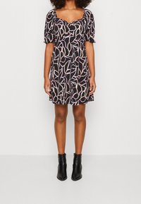 Femme portant une robe noire longueur genou avec un imprimé abstrait rose et des manches bouffantes, associée à des bottines noires.