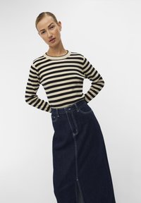 Pull rayé beige et noir, associé à une jupe maxi en denim foncé avec une fente frontale et des détails de couture visibles.