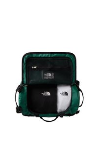 Green fabric bag with a zippered mesh pocket. Contains two folded shirts, one black and one white, both displaying a logo.