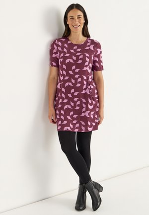 Lila kortärmad klänning med rosa abstrakt mönster, med sidofickor och en avslappnad passform, i kombination med svarta leggings och ankelstövlar.