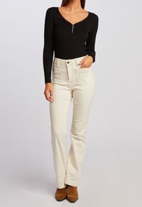 Haut noir côtelé à manches longues avec un col zippé, associé à un pantalon crème taille haute avec poches avant et une texture subtile.