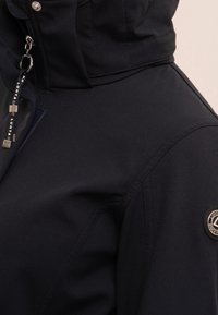 Marine softshell jas met een hoge kraag, ritsdetails, gemerkte hardware en een gestructureerde stof met strakke naden voor een atletische pasvorm.