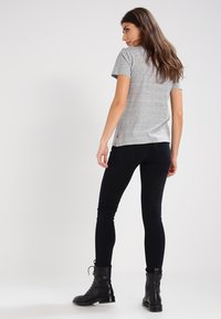 Grå t-shirt med korte ærmer vist fra ryggen, parret med sorte skinny jeans og sorte snørede støvler. Enkel design uden mønstre.