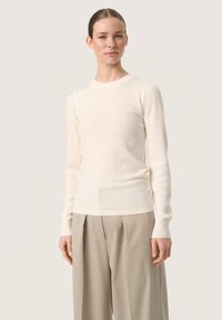 Cream ribbed knit sweater with long sleeves, round neckline, and fitted cuffs, paired with high-waisted beige trousers.