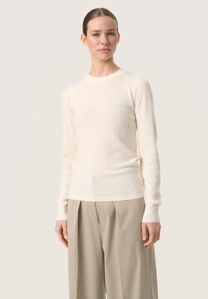 Crème kleurige ribgebreide trui met lange mouwen, ronde halslijn en aangesloten manchetten, gecombineerd met hooggesneden beige broeken.