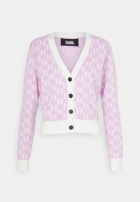 Růžový pletený kardigan s bílými akcenty, s opakujícím se vzorem "K", výstřihem do V a černými knoflíky. Zkrácený střih s dlouhými rukávy.