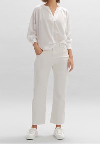 Blusa blanca de manga larga con escote partido, combinada con pantalones blancos de pierna recta. Calzado: zapatillas blancas. Diseño sencillo, textura suave.