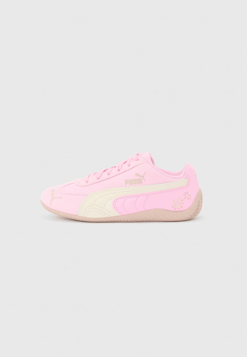 Jasnoróżowy sneaker Puma z beżową podeszwą, beżowym paskiem, sznurówkami i kwiatowymi zdobieniami na pięcie, przedstawiony z profilu na jasnym tle.