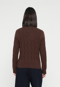 Brun strikket genser med kabelmønster, ribbestrikket kant og mansjetter, lange ermer og rund hals, sett fra baksiden.