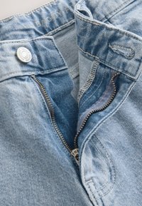 Light blue denim jeans featuring a zippered fly, metal button closure, and visible stitching details. The fabric has a slightly worn texture.