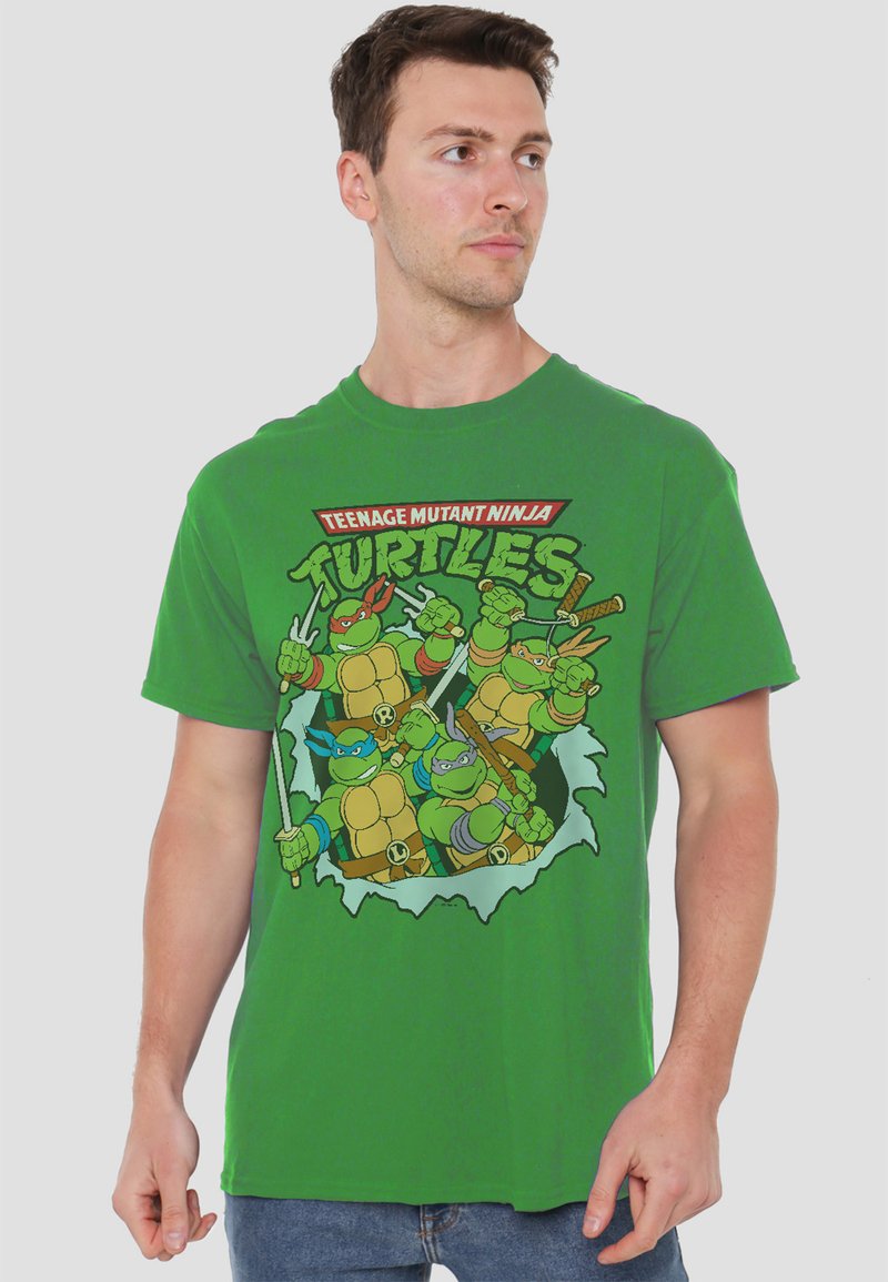 Green cotton T-shirt featuring a graphic of four cartoon turtles breaking through a wall, with vibrant colors and bold text above.