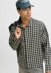 Schwarz-weiße karierte Button-up-Hemd mit Kragen, kombiniert mit einer dunklen Kappe mit weißem Text. Strukturiertes Gewebe mit sichtbaren Nähten.