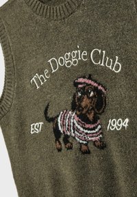 Olivgrön kofta utan ärmar med ribbad halsringning, prydd med en svart och brun broderad tax i randig tröja, texten "The Doggie Club EST 1994."