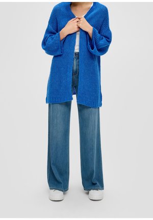 Open-front cardigan van levendig blauwe brei fabric; heeft lange mouwen en een losse pasvorm. Gecombineerd met brede denim jeans en witte sneakers.