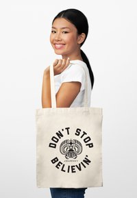 Bolsa de tela de algodón beige con el texto gráfico negro "NO DEJES DE CREER" y un diseño intrincado. Asa larga para un fácil transporte.