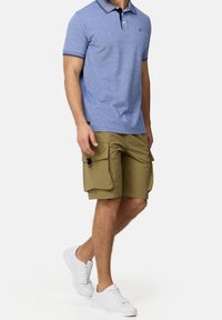 Polo bleu avec un col marine, associé à un short cargo beige avec des poches latérales. Porté avec des baskets blanches.