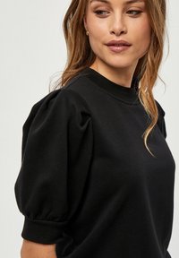 Svart sweatshirt med puffiga korta ärmar, rund halsringning och mjuk textur. Rent design utan synliga mönster eller detaljer.