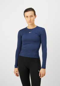 Dug součanika, tamnoplavi sportski majica dugih rukava od rastezljivog materijala, s okruglim izrezom i malim bijelim Nike logom na prsima.
