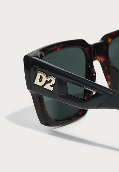 Black and tortoiseshell sunglasses with green lenses, featuring a prominent gold "D2" logo on the side and angular frame design.