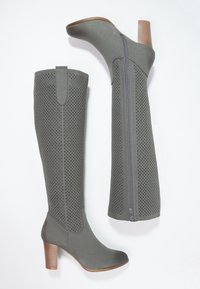 Bottes grises montantes jusqu'au genou avec tige perforée, fermeture éclair latérale et talon bloc. Texture lisse avec une semelle extérieure en caoutchouc beige.
