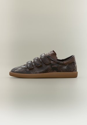 Baskets basses avec texture cuir de serpent marron, trois bandes velcro et semelle marron clair sur fond neutre.