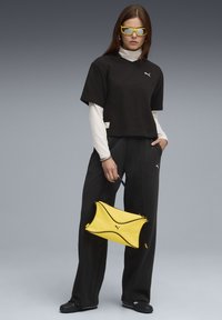 Sort cropped top med korte ærmer, parret med løse sorte bukser. En lys gul håndtaske med sort kant, cylindriske solbriller og sneakers.
