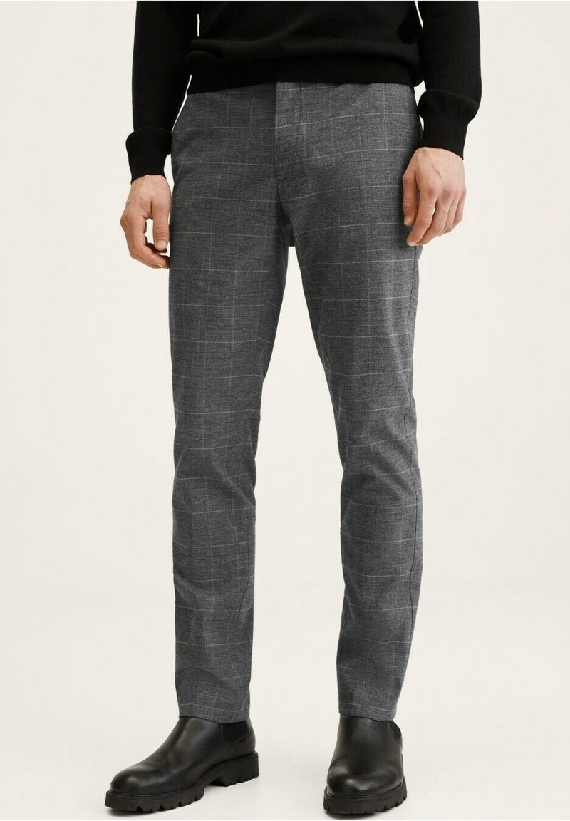 Grijze geruite broek met een slim fit, gemaakt van een gestructureerde stof en een subtiel ruitpatroon, gecombineerd met zwarte enkellaarsjes.