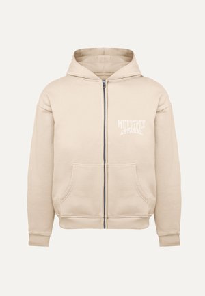Felpa beigi con zip realizzata in tessuto morbido, con cappuccio regolabile, tasche frontali e un piccolo logo bianco nella zona sinistra del petto.