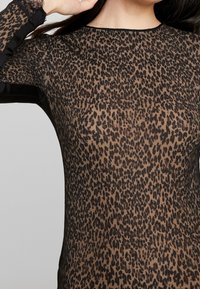 Top i leopardmönster med genomskinligt brunt tyg, svarta detaljer och rund halsringning. Långa ärmar med fransigt detaljer vid ärmsluten.