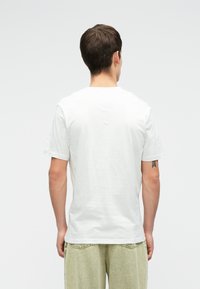 Bela bomba majica iz bombaža s kratkimi rokavi, okroglo izrezom in gladko teksturo. Oblečena z ohlapnimi svetlo zelenimi hlačami z karo pasom.