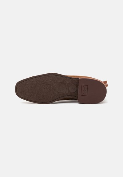 Fondo de zapato de ante marrón con una suela de goma texturizada. Presenta una etiqueta de logo rectangular y un pequeño tacón con una lengüeta.