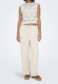 White crochet tank top with scalloped edges, paired with loose-fitting, light beige linen pants, and brown espadrille sandals.