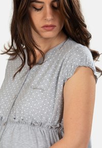 Blusa grigia a pois con maniche corte a palloncino, scollatura a V e vita arricciata. Presenta una delicata ricamo nella zona del petto.