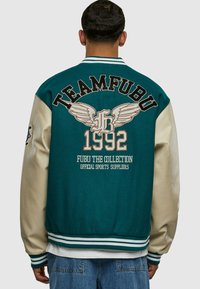 Teal a krémová varsity bunda s vyšitým designem "TEAMFUBU" a křídel, žebrované manžety a pas, vyrobená z kombinace materiálů.