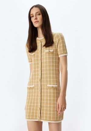 Robe à manches courtes en motif à carreaux jaune et blanc, avec un devant à boutons, un tissu texturé et deux poches à rabat avec une bordure.