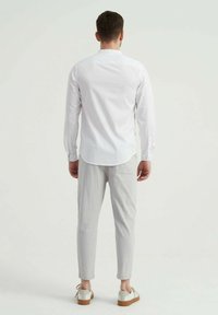 Chemise blanche à manches longues, coupe slim. Pantalon texturé gris clair avec poches latérales, associé à des baskets blanches avec semelles marron.