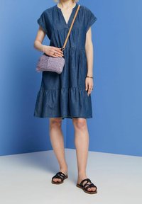 Denim dress with short sleeves, gathered tiers, and a V-neck; paired with a crocheted purple bag and black strappy sandals.