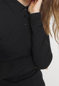 Schwarz geripptes Langarm-Polohemd mit Kragen und dreiknöpfiger Knopfleiste, mit einer strukturierten Oberfläche und enganliegenden Ärmeln.